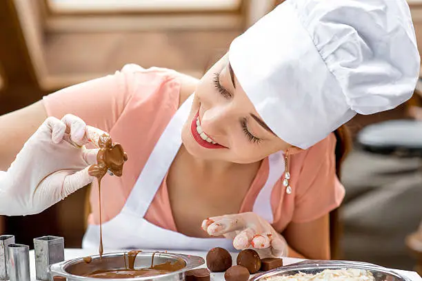 Young smiling woman chef dressed in white pinafore making handmade chocolate candy in the cafe
