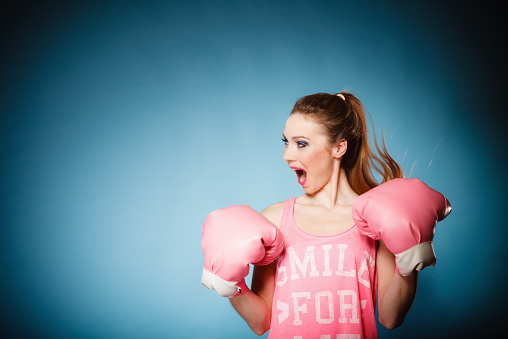 Funny girl female boxer model wearing big fun pink gloves playing sports boxing studio shot blue background