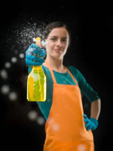 portrait of cleaning woman aiming spray bottle in front of her, on black background