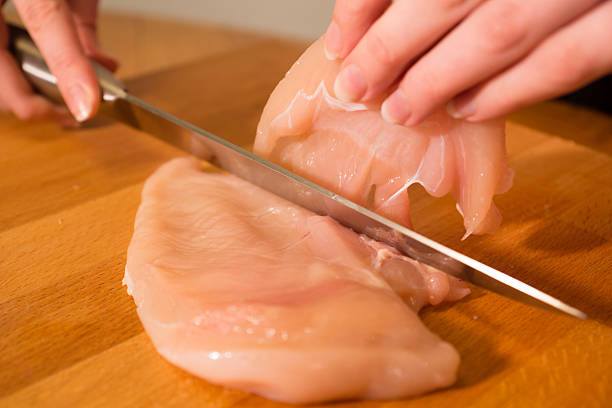 Chicken breast meat being sliced with a knife by beautiful woman hands.