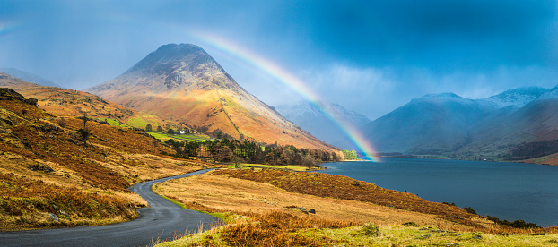 Colourful rainbow soaring over the blue shore of Wast Water and Yewbarrow overlooed by the snowy peaks of Great Gable and Scafell in this picturesque panoramic vista of the Lake District National Park, Cumbria, UK. ProPhoto RGB profile for maximum color fidelity and gamut.