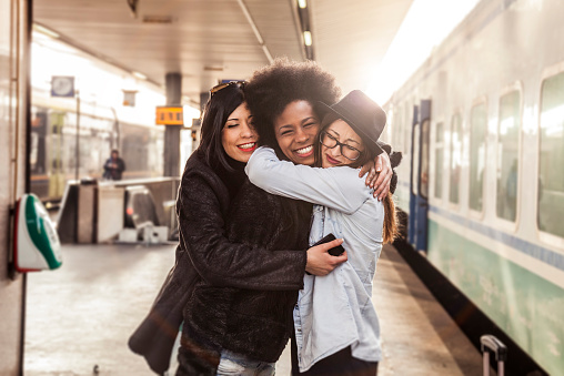 Three women friends greet at the train station before leaving for vacations