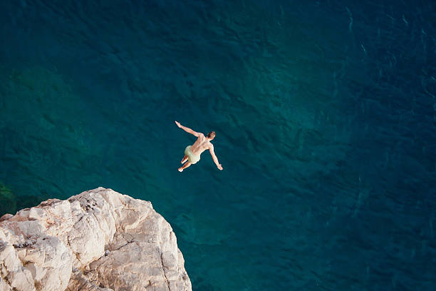 jeune homme sauter de la falaise dans la mer. - extreme sports high up sport outdoors photos et images de collection