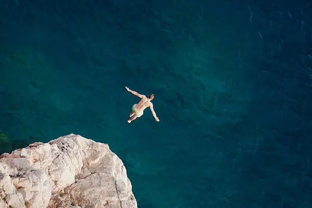 Young man jumping from cliff into sea