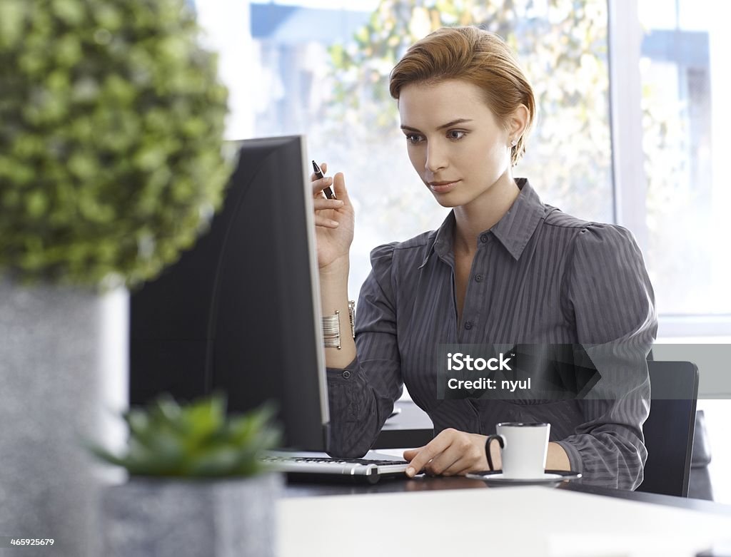 Attractive businesswoman working with computer Attractive young businesswoman working with computer, sitting at desk, concentrating. Green plants in foreground.. 20-24 Years Stock Photo