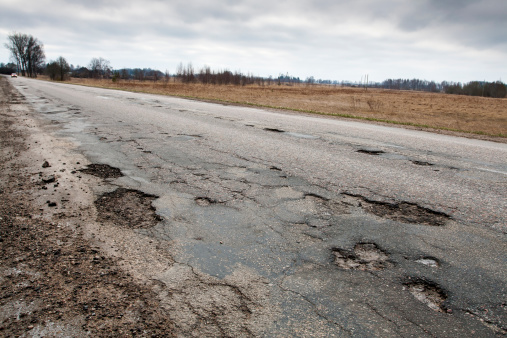 Badly damaged country asphalt road after winter