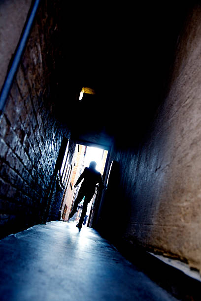 Mysterious running man A mysterious running man silhouetted in a dark alleyway. detective wall stock pictures, royalty-free photos & images