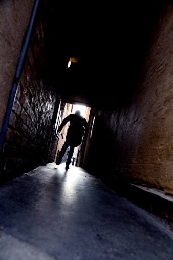 A mysterious running man silhouetted in a dark alleyway.