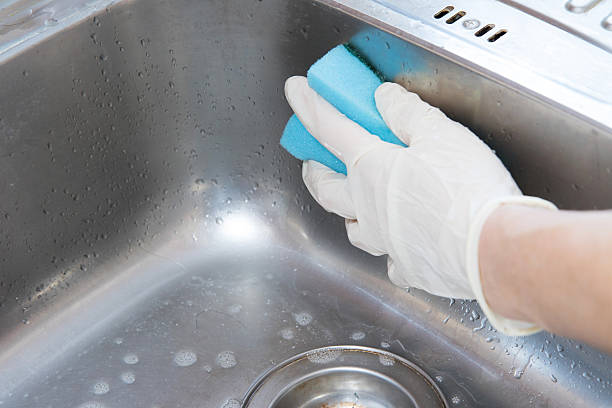 istock Hand in white glove cleaning kitchen sink with blue sponge 465944108