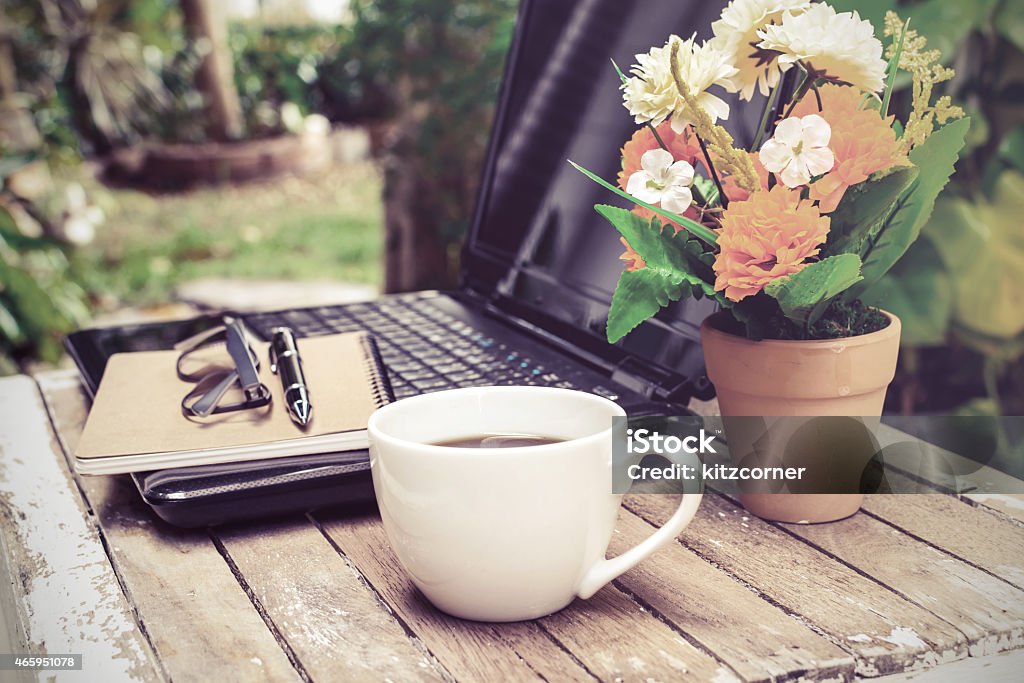 Arrangement of outdoor work station with laptop, coffee cup of coffee and laptop on wooden table with flower and notebook in the garden, Vintage style 2015 Stock Photo