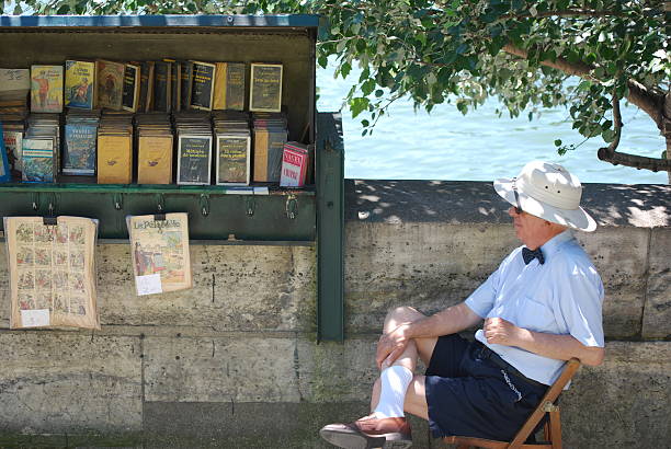 Paris, France - June 5, 2014: A buquiniste waiting for people to come to visit his green box full of French books and magazines.