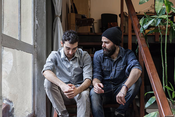 deux jeunes hommes parler dans l'escalier - unsmiling photos et images de collection
