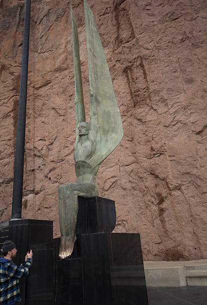 Hoover Dam Statue Boulder City, United States - February 23, 2015: This image shows a man photographing a metal statue at Hoover Dam, a concrete arch gravity dam on the Colorado River on the border of Nevada and Arizona.  hoover dam statues stock pictures, royalty-free photos & images