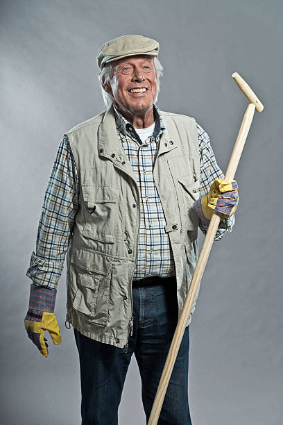 istock Smiling senior gardener man with hat holding hoe. Studio shot. 465971441