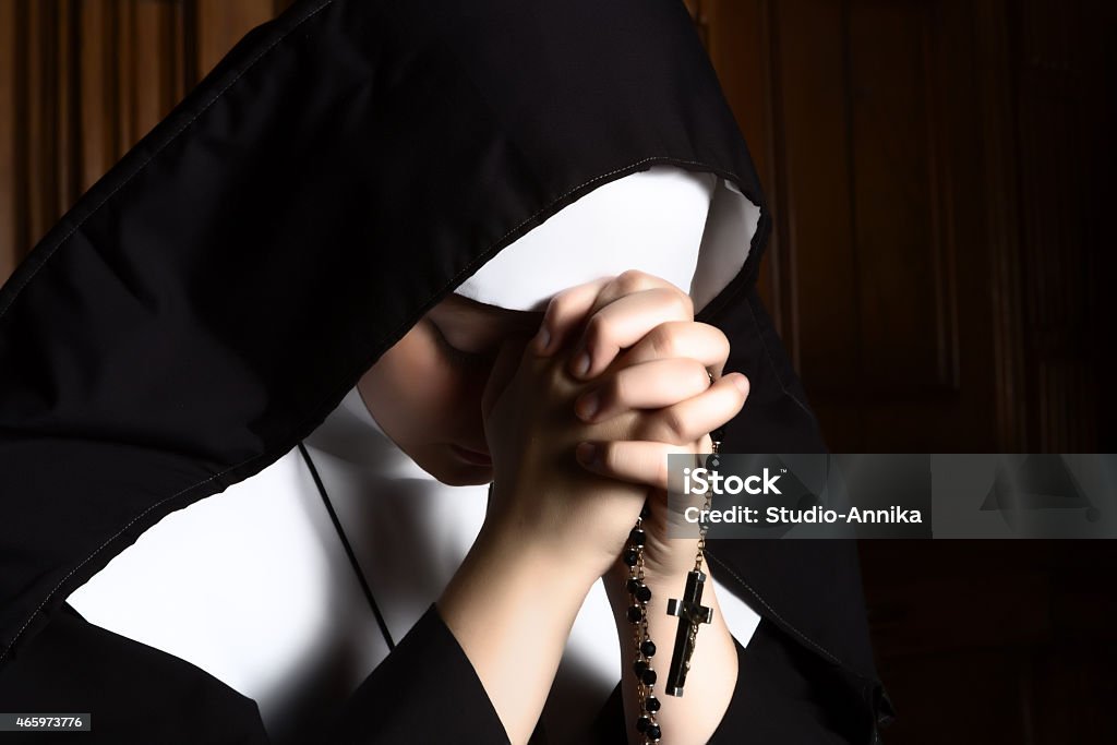 Nun folding hands holding a rosary praying Fine art portrait of a novice nun in deep prayer with rosary Nun Stock Photo