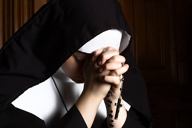 Nun folding hands holding a rosary praying stock photo