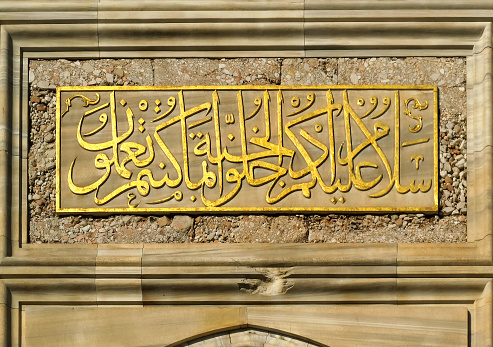 Enlightened by sun, golden text in arabic script above the door of the Süleymaniye Mosque in turkish Istanbul.