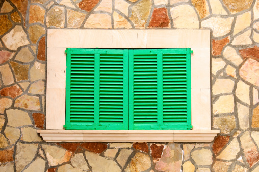 Closed green wooden window shutters framed by a stone wall.