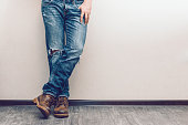 Mans legs in jeans and boots leaning on a white wall