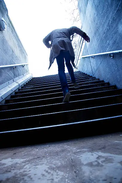 A mysterious man running up stone stairs, in an urban setting.