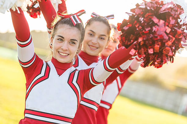 istock Three smiling cheerleaders with raised pompoms outside 466003411
