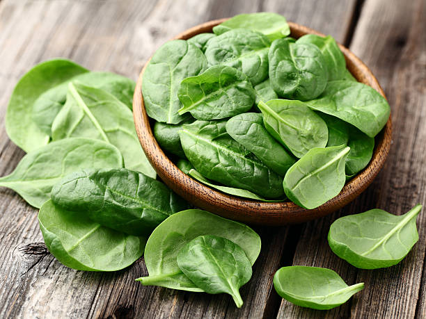 Fresh baby spinach leaves in a bowl on a wooden table stock photo