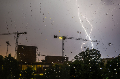 Lightning strike in a construction area viewed through glass with rain drops.