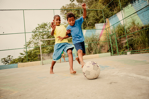 Two boys from the favelas in Rio de Janeiro challenge each other for the soccer ball on a concrete pitch.