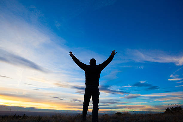 istock silhouette man arms raised into sunset sky landscape 466016545