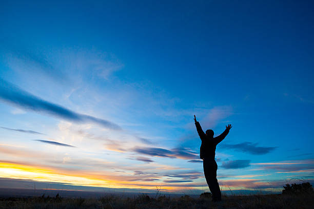 istock silhouette man arms raised into sunset sky landscape 466016547