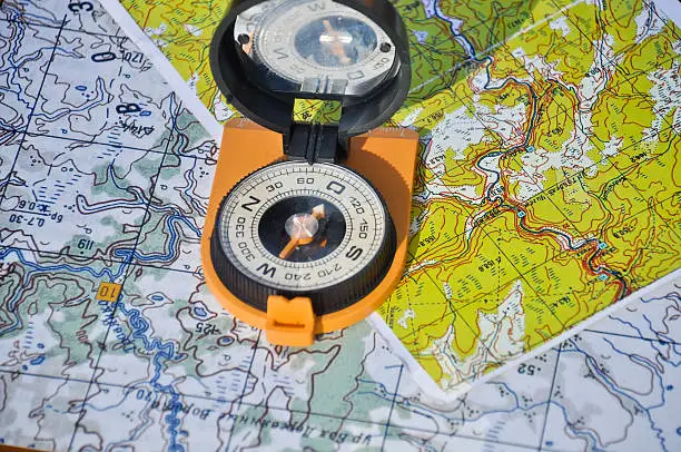 Orange compass mirror cover lies on topographic maps. Compass on the map