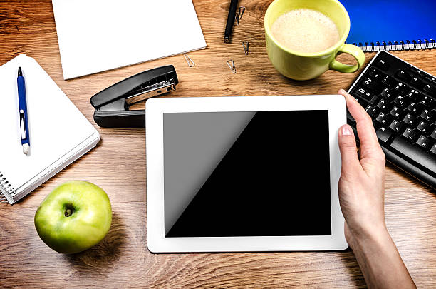 Tablet with an empty screen in hands close to a pen and green cup