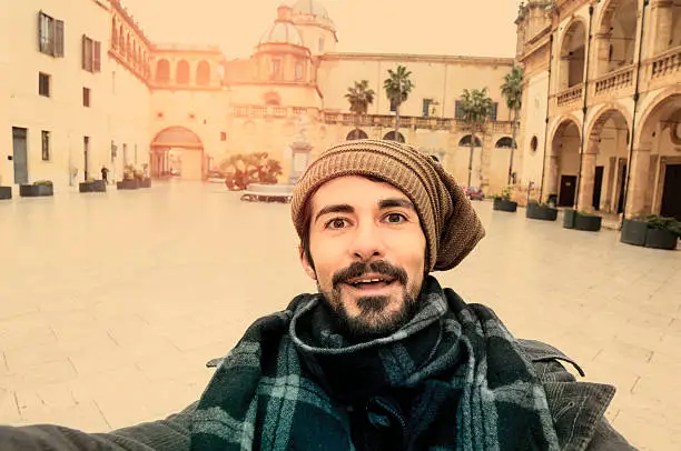 Young Man Taking Selfie in a euroepan square with a church on the background in instagram toned style