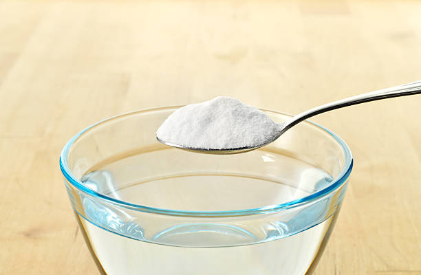 Close-up of baking soda on spoon. Close-up of baking soda on spoon against background of glass of water on wooden table. Bicarbonate of soda. Copy space. sodium stock pictures, royalty-free photos & images