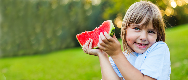Little girl smiling and eating watermelon fruit outdoors