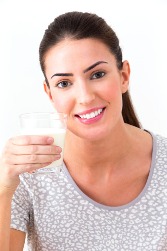 A woman holds out a glass of fresh milk and smiles