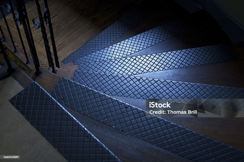 curved steps Metel traction strips on wooden stairway curving downward illuminated by light through a small window. Angle Stock Photo