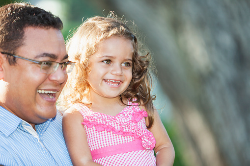 Hispanic preschool girl (2-3 years) with father (40s) outdoors.  Main focus on girl.