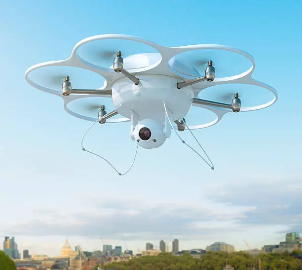This image features a clear and realistic scene showing a drone hovering over a mixed area of nature and city as a low backdrop at the bottom of the frame.  The drone is centered between six individual rotating blades, each within its own support cylinder.  All of the blades are working together to keep the drone