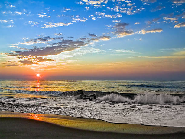 The sun rises over vreaking waves on the beach at Fenwidk Island, Delaware.