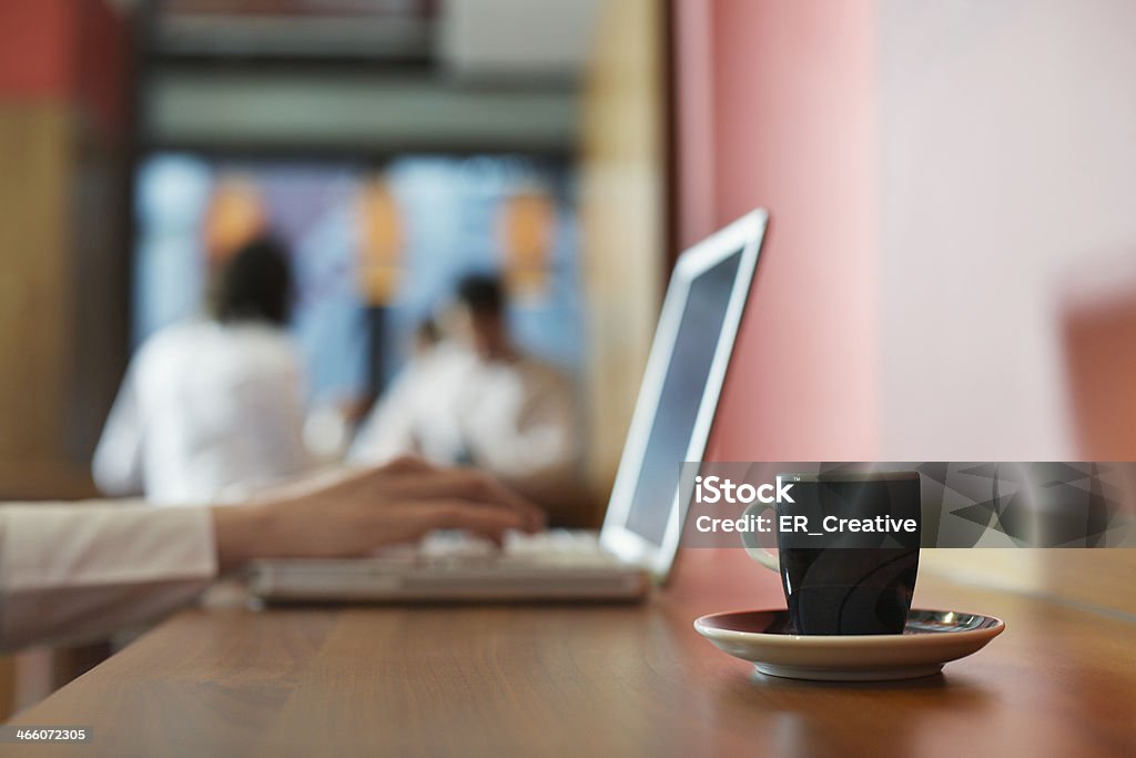 Young businesswoman with laptop and cup of coffee Businesswoman sitting and working at cafe during coffee break, her colleagues sitting background Adult Stock Photo