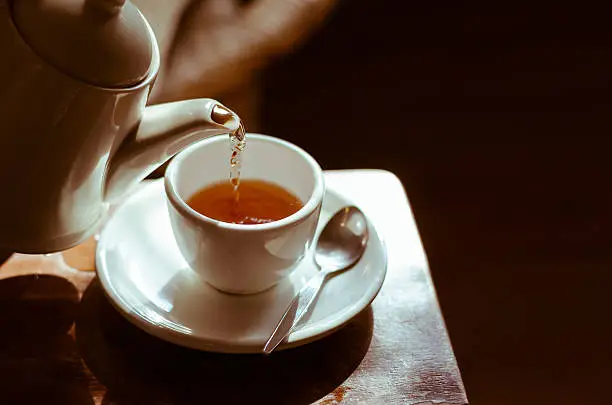 Pouring hot tea into white ceramic tea cup the time of tea break.