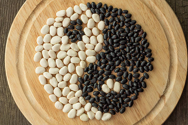 Yin and yang of black and white beans on wooden plate