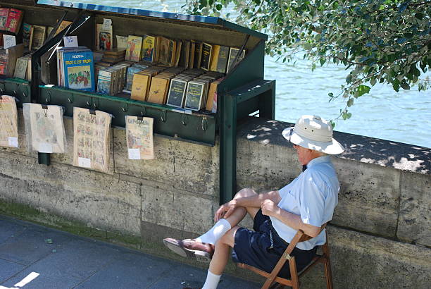 Paris, France – June 5, 2014: A buquiniste man waiting for people to come to visit his green box full of French books and magazines.