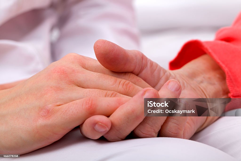 Person in red holding another person's hand over white Caregiver holding elderly patients hand at home 2015 Stock Photo