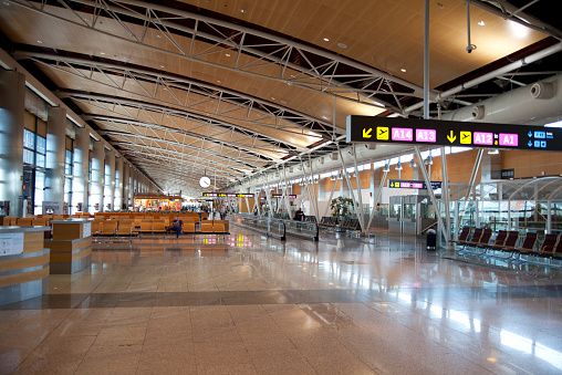Interior of Madrid airport, departure waiting aria with glossy floor reflecting the lights, clock and shops in distant and lots of people