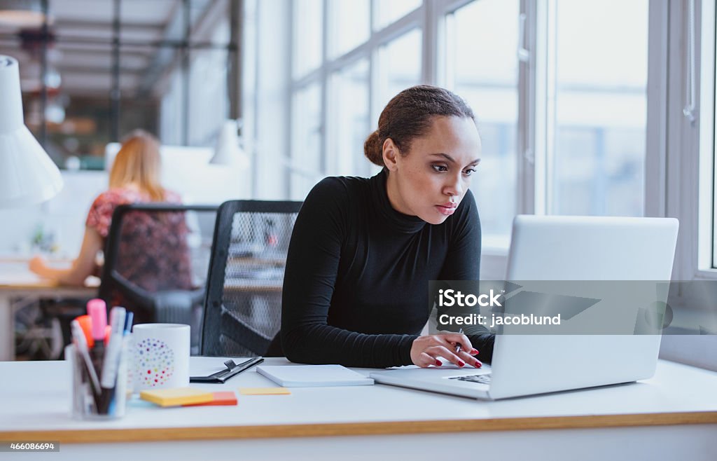 Young business executive using laptop Image of woman using laptop while sitting at her desk. Young african american businesswoman sitting in the office and working on laptop. Office Stock Photo