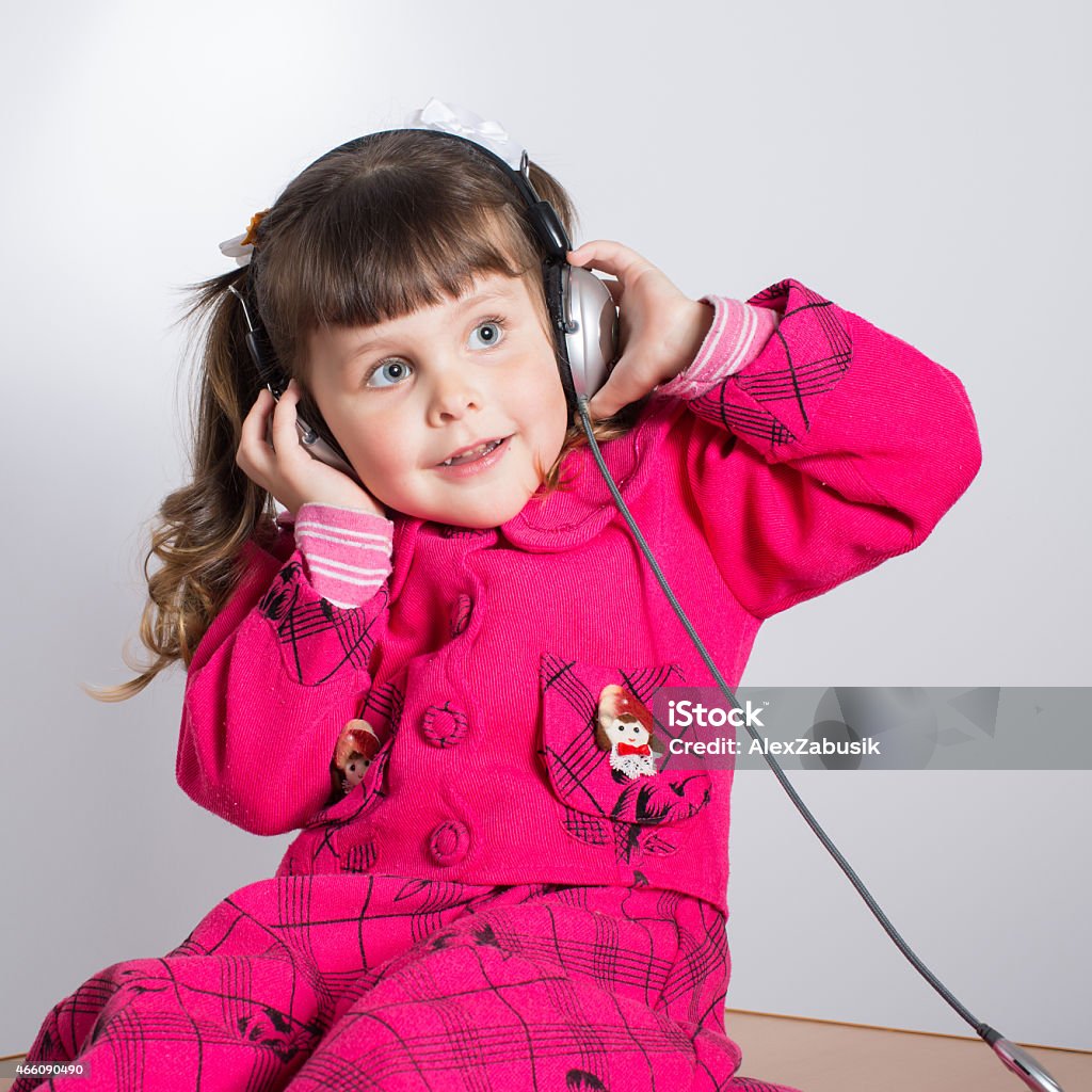 Preschooler girl in headphones Portrait of preschooler girl in headphones. Charming child in pink dress indoors. Studio shot 2-3 Years Stock Photo