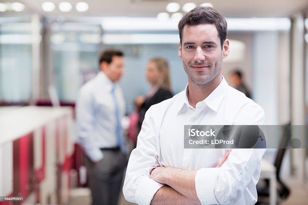 Empresario sonriente posando mientras sus colegas hablando juntos en el fondo - Foto de stock de Ejecutivo libre de derechos