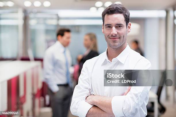 Empresario Sonriente Posando Mientras Sus Colegas Hablando Juntos En El Fondo Foto de stock y más banco de imágenes de Ejecutivo